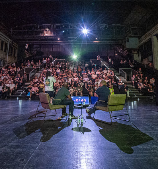 A stage with two men having a discussion panel in front of an audience